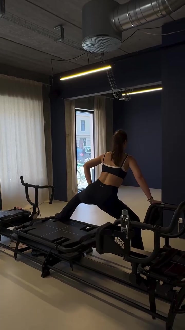 Face-away client using a Megaformer beside the studio mirror and machine row.