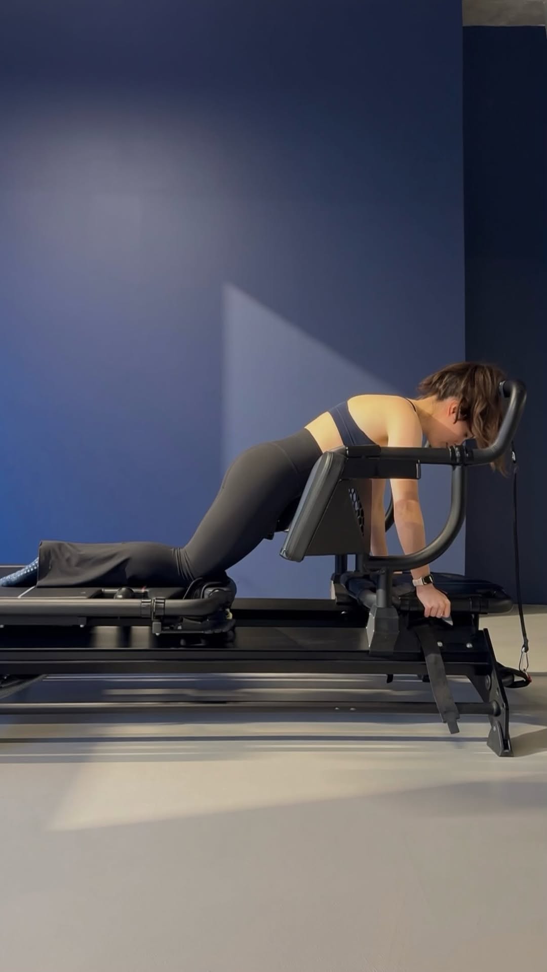 Face-hidden client in a slow wheelbarrow position showing the full black Megaformer side profile.